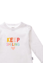 Detailansicht des Baumwollshirts in weiß mit buntem Keep Smiling Print. Das Shirt hat praktische Druckknöpfe für ein einfaches an und ausziehen.