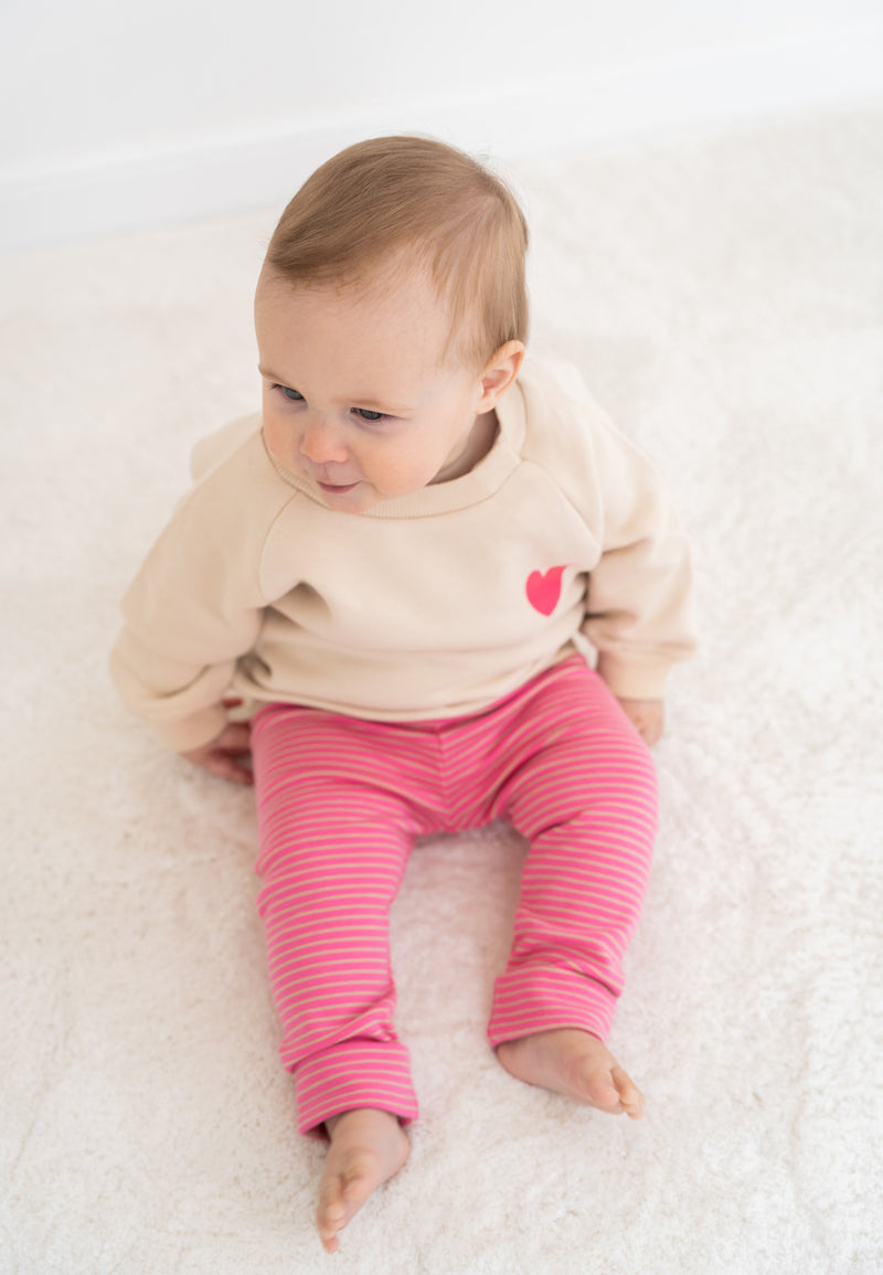 2-teiliges Baby Set mit beigem Sweatshirt mit pinkem Herz-Print und pink-rosa gestreifter Leggings, flach auf weißem Hintergrund
