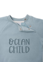 Detailaufnahme des Prints "Ocean Child" und praktischen Druckknöpfen am Halsausschnitt für die Größen 74/80 und 86/92.